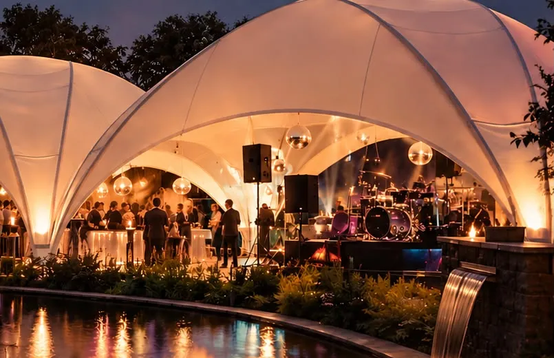 Linked crossover domes glowing warm white at night, with a band and bar set up underneath